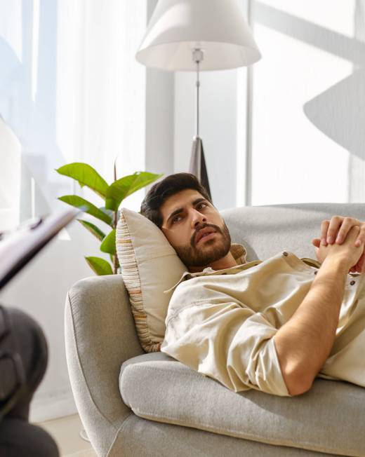 Pensive depressed man frowning looking at therapist lying on sofa in office cabinet